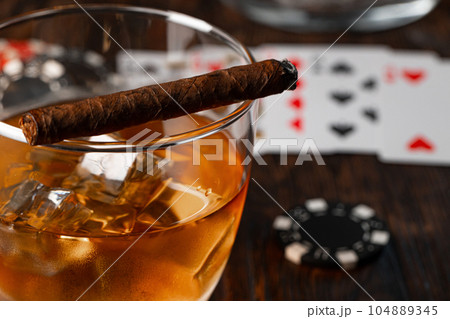 Cuban cigar, whiskey glass and chips on table 104889345