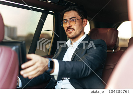 Young elegant businessman watching TV on the screen in luxury car 104889762