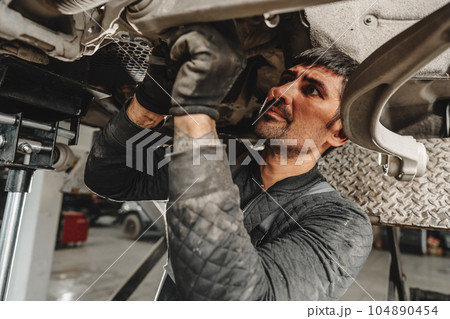 Auto mechanic repairs running gear of a car in car service Auto mechanic repairs running gear of a car in car service 104890454