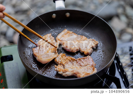キャンプで豚肉を焼く男性　ガスコンロ 104890656