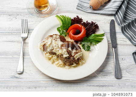 Two beef patties with sauce and fresh vegetables served on plate in cafe 104891073