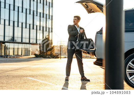 Successful businessman taking luggage from the car trunk Successful businessman taking luggage from the car trunk 104891083
