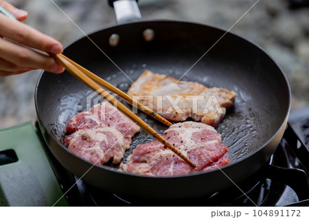 キャンプで豚肉を焼く男性　ガスコンロ 104891172