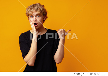 Handsome young man pointing finger to copy space on yellow banner background 104892080
