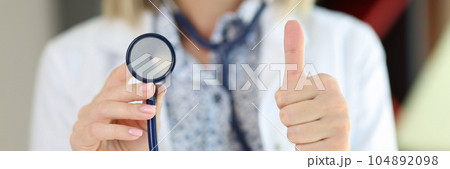 Cropped view of female doctor holding stethoscope and showing thumbs up. Cropped view of female doctor holding stethoscope and showing thumbs up. 104892098