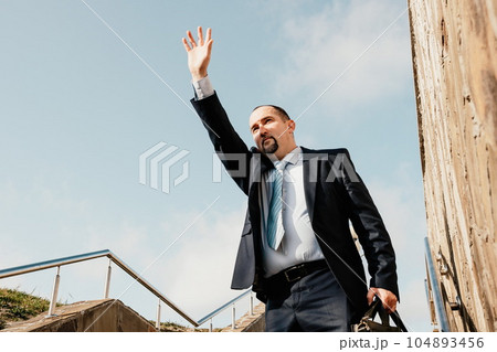 Confident middle age businessman with briefcase walking upstairs. Close-up of businessman wearing blue suit holding bag walking down the stairs 104893456
