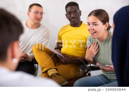 Cheerful young girl talking to colleagues in office lounge during break Cheerful young girl talking to colleagues in office lounge during break 104893644