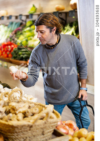 Adult man buyer chooses garlic in shop Adult man buyer chooses garlic in shop 104893688