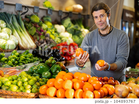 Man diligently picking out mandarin orange to buy in vegetable aisle of supermarket Man diligently picking out mandarin orange to buy in vegetable aisle of supermarket 104893767