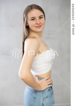 Portrait of young girl in tank top and jeans on gray background Portrait of young girl in tank top and jeans on gray background 104894049
