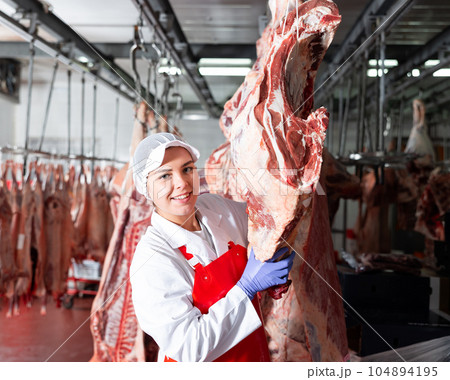 Female slaughterhouse worker showing beef chunk in meat storage 104894195