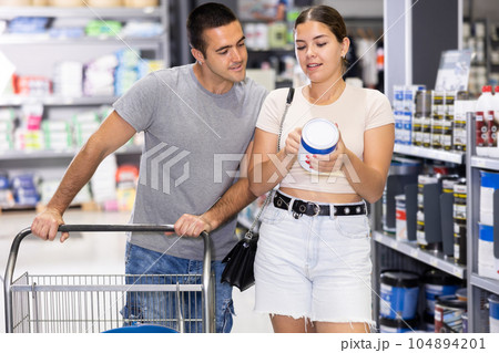Smiling couple talking while choosing paints in construction hypermarket Smiling couple talking while choosing paints in construction hypermarket 104894201