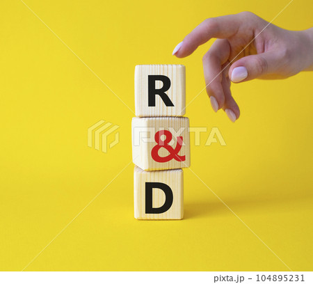 R and D - research and development symbol. Wooden cubes with word R and D. Businessman hand. Beautiful yellow background. Business and R and D concept. Copy space. 104895231