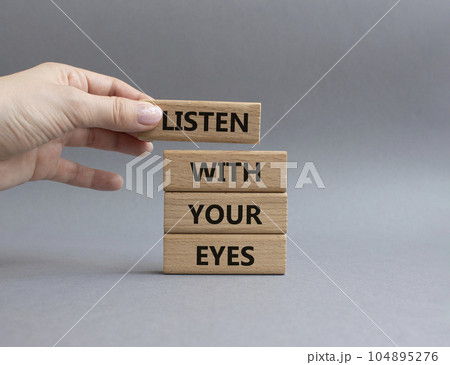 Listen with your eyes symbol. Concept word Listen with your eyes on wooden blocks. Beautiful grey background. Businessman hand. Business and Listen with your eyes concept. Copy space 104895276