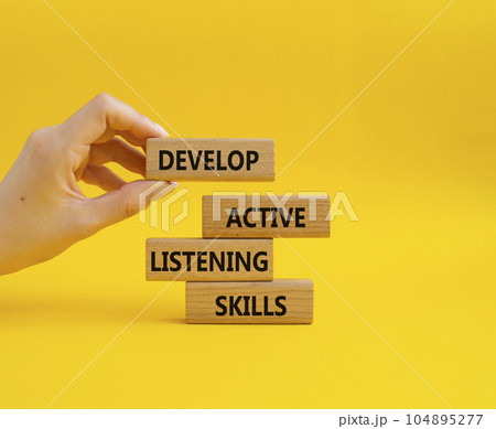 Listening skills symbol. Concept word Develop active listening skills on wooden blocks. Beautiful yellow background. Businessman hand. Business and Develop active listening skills concept. Copy space 104895277