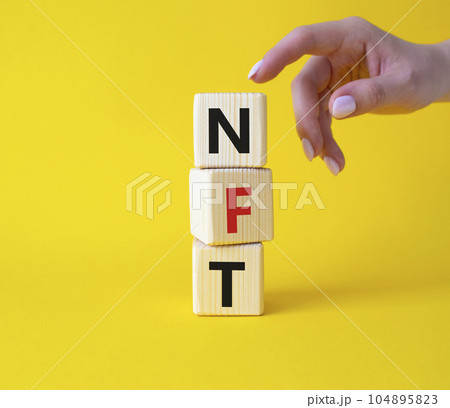 NFT - non-fungible token symbol. Concept word NFT on wooden cubes. Businessman hand. Beautiful yellow background. Business and NFT concept. Copy space. NFT - non-fungible token symbol. Concept word NFT on wooden cubes. Businessman hand. Beautiful yellow background. Business and NFT concept. Copy space. 104895823