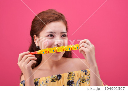 female model in a flower-patterned dress playing a toy flute on a pink background 104901507