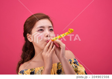 female model in a flower-patterned dress playing a toy flute on a pink background 104901508
