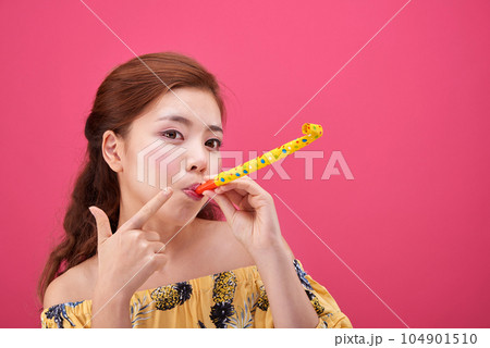 female model in a flower-patterned dress playing a toy flute on a pink background 104901510