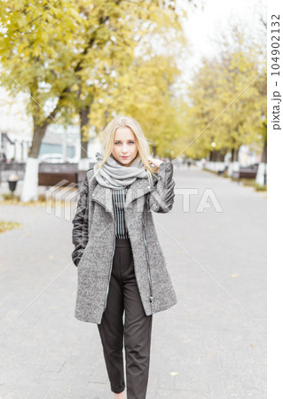 A young blonde walks through the autumn city in a gray coat. The concept of urban style and lifestyle. 104902132
