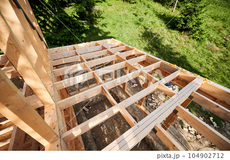 Under-construction residential wooden frame building. Initiation of new construction project for cozy mountain cottage. The concept of modern ecological construction and contemporary architecture. Under-construction residential wooden frame building. Initiation of new construction project for cozy mountain cottage. The concept of modern ecological construction and contemporary architecture. 104902712