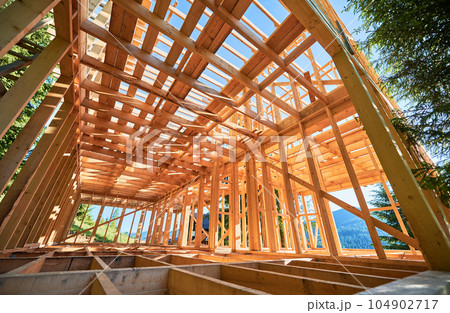Under-construction residential wooden frame home located near a forest. Commencement of a new construction project for a cozy house or a mountain cottage. Idea of contemporary ecological construction. 104902717