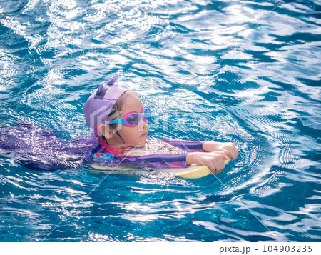 Asian child or kid girl wearing swimming suit to learning on swimming pool , learn and training swim on kick board Asian child or kid girl wearing swimming suit to learning on swimming pool , learn and training swim on kick board 104903235