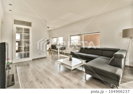 a living room with wood flooring and white walls, there is a black couch in the center of the room a living room with wood flooring and white walls, there is a black couch in the center of the room 104906237