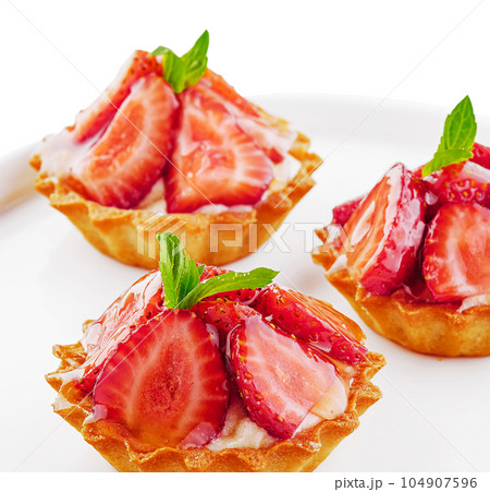 Tartlets with custard, strawberries and mint served on white plate Tartlets with custard, strawberries and mint served on white plate 104907596