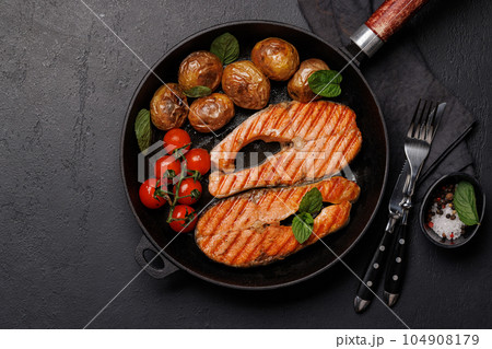 Grilled salmon steaks and potatoes sizzling in a frying pan 104908179