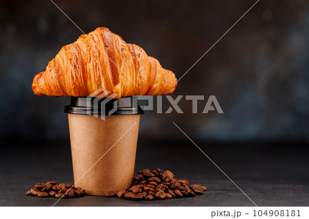 Aromatic coffee in a paper cup paired with a flaky croissant 104908181