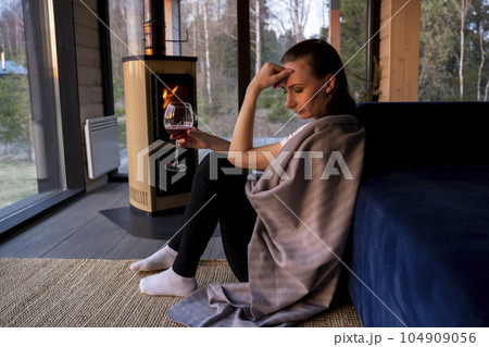 Young beautiful woman in depression, drinking alcohol, is sitting by the sofa near the fireplace in the living room 104909056