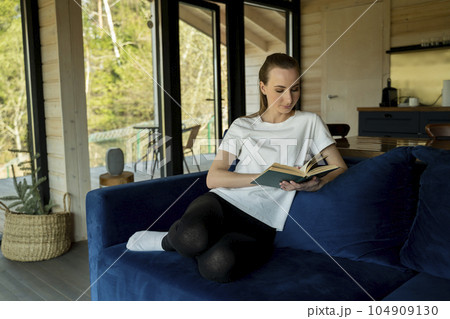 Attractive young woman sits in the minimal and comfortable living room enjoying reading a book. Attractive young woman sits in the minimal and comfortable living room enjoying reading a book. 104909130