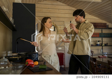 Infidelity. A jealous husband shows his cheating wife her phone, demanding an explanation, standing in the kitchen. Husband caught his wife cheating with a mobile phone - divorcing people 104909131