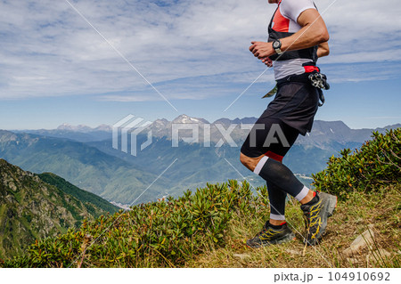 male athlete running from mountainside in compression sleeves on his feet in mountain marathon race 104910692