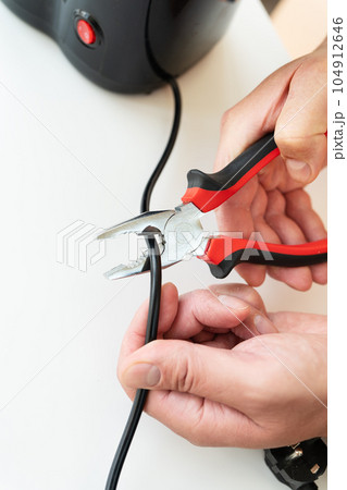 A man sits at a table and makes repairs to small household appliances, repairs with a screwdriver. Close-up. A man sits at a table and makes repairs to small household appliances, repairs with a screwdriver. Close-up. 104912646