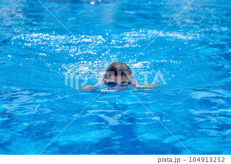 Fit swimmer training in the swimming pool. An overhead view of a man diving into a pool, forming an arrow shape and leaving a trail behind him. Professional male swimmer inside swimming pool. Young Fit swimmer training in the swimming pool. An overhead view of a man diving into a pool, forming an arrow shape and leaving a trail behind him. Professional male swimmer inside swimming pool. Young 104913252