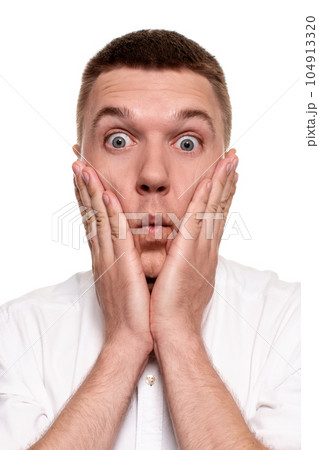 Portrait of bothered handsome young man in white shirt holding palms near cheek Portrait of bothered handsome young man in white shirt holding palms near cheek 104913320