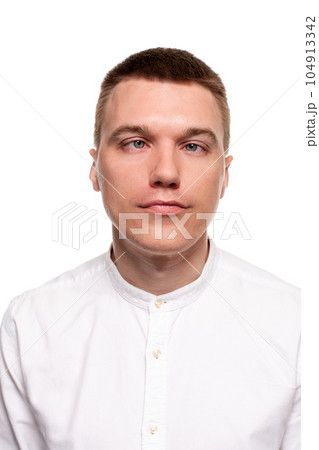 Charming handsome young man in a white shirt is making faces, while standing isolated on a white background Charming handsome young man in a white shirt is making faces, while standing isolated on a white background 104913342