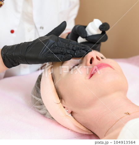 The beautician presses on a jar of cream that drips onto the girl's face. 104913564
