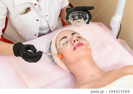 The cosmetologist applies a liquid gel to the face with a wide brush 104913569