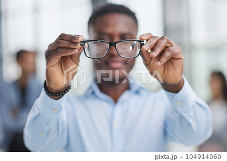a black man in a blue shirt adjusts his glasses. a black man in a blue shirt adjusts his glasses. 104914060