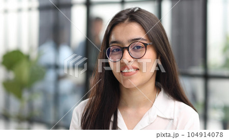 Close-up portrait of a confident and attractive woman in a white blouse and glasses in a classroom or office. 104914078