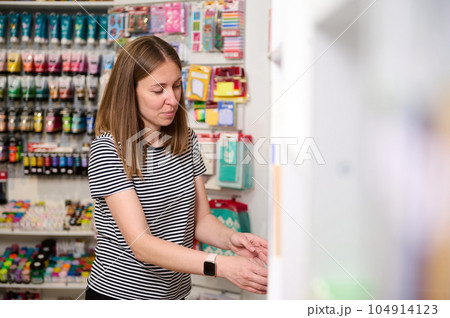 Pleasant female seller in office supply shop, stacking school supplies on display shelves, working on merchandising 104914123