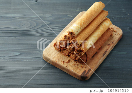Waffle tubes with chocolate filling on wooden board Waffle tubes with chocolate filling on wooden board 104914519