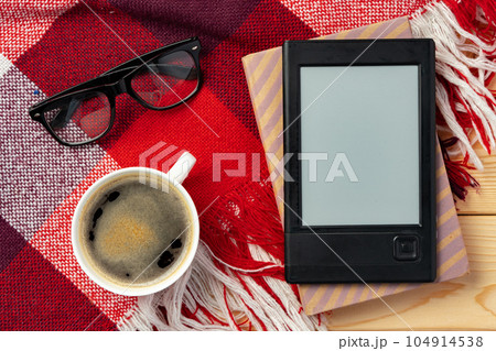 E-book reader and cup of coffee on knit plaid background E-book reader and cup of coffee on knit plaid background 104914538