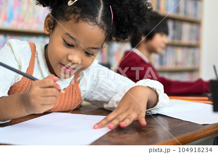 Cute pupils writing and painting on paper at desk in classroom 104918234