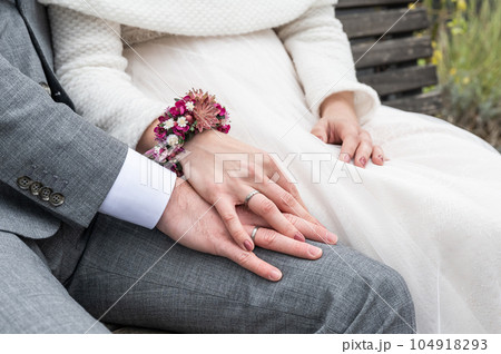 Bride holding groom hand with wedding rings sitting on bench Bride holding groom hand with wedding rings sitting on bench 104918293