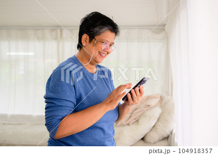 Healthy mature woman holding smartphone using mobile app and chatting with friends, Senior people with technology at home, Grandmother relaxing at home with happiness 104918357