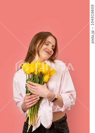 Happy young european lady holds bouquet of yellow tulips with closed eyes, pink background. Gift to women day. Mother day. March 8. Happy young european lady holds bouquet of yellow tulips with closed eyes, pink background. Gift to women day. Mother day. March 8. 104919609